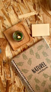 Overhead view of a rustic desk with a Naturel notebook and candle, perfect for a tranquil workspace.